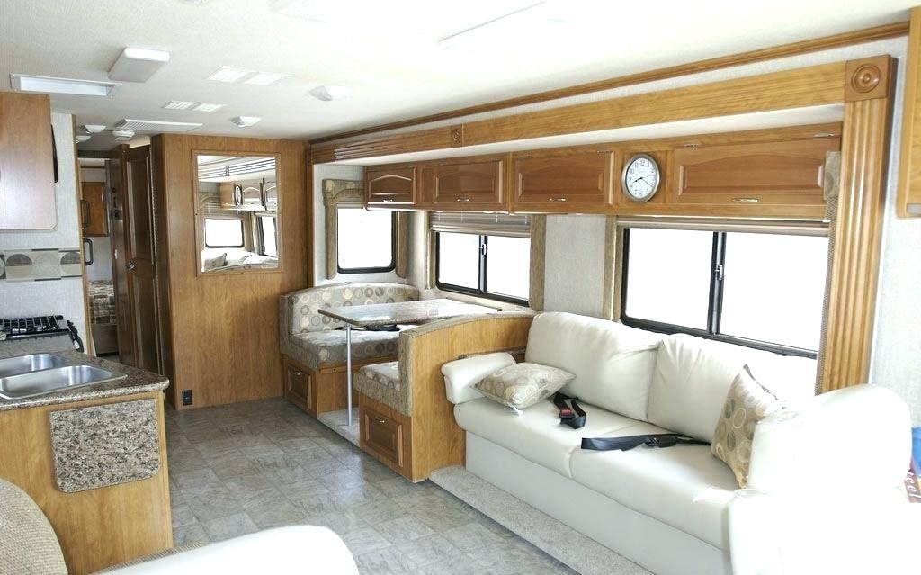 There is the inside of a larger RV. There is a big couch with seatbelts as well as a sink and table.