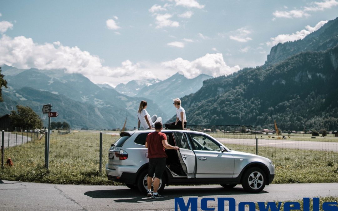 Three people sitting on an SUV with mountains in the background