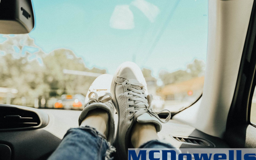 A pair of white lace-up shoes being kicked up on the dash of a car.