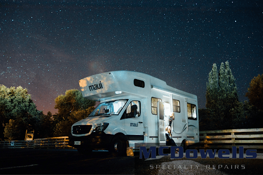 A white RV parked against a wooden fence. The background is a starry sky.